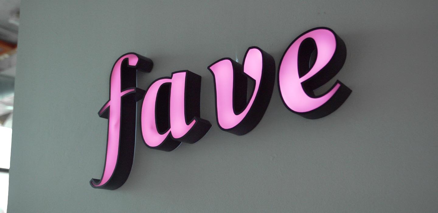 Pink neon Fave logo on a white wall