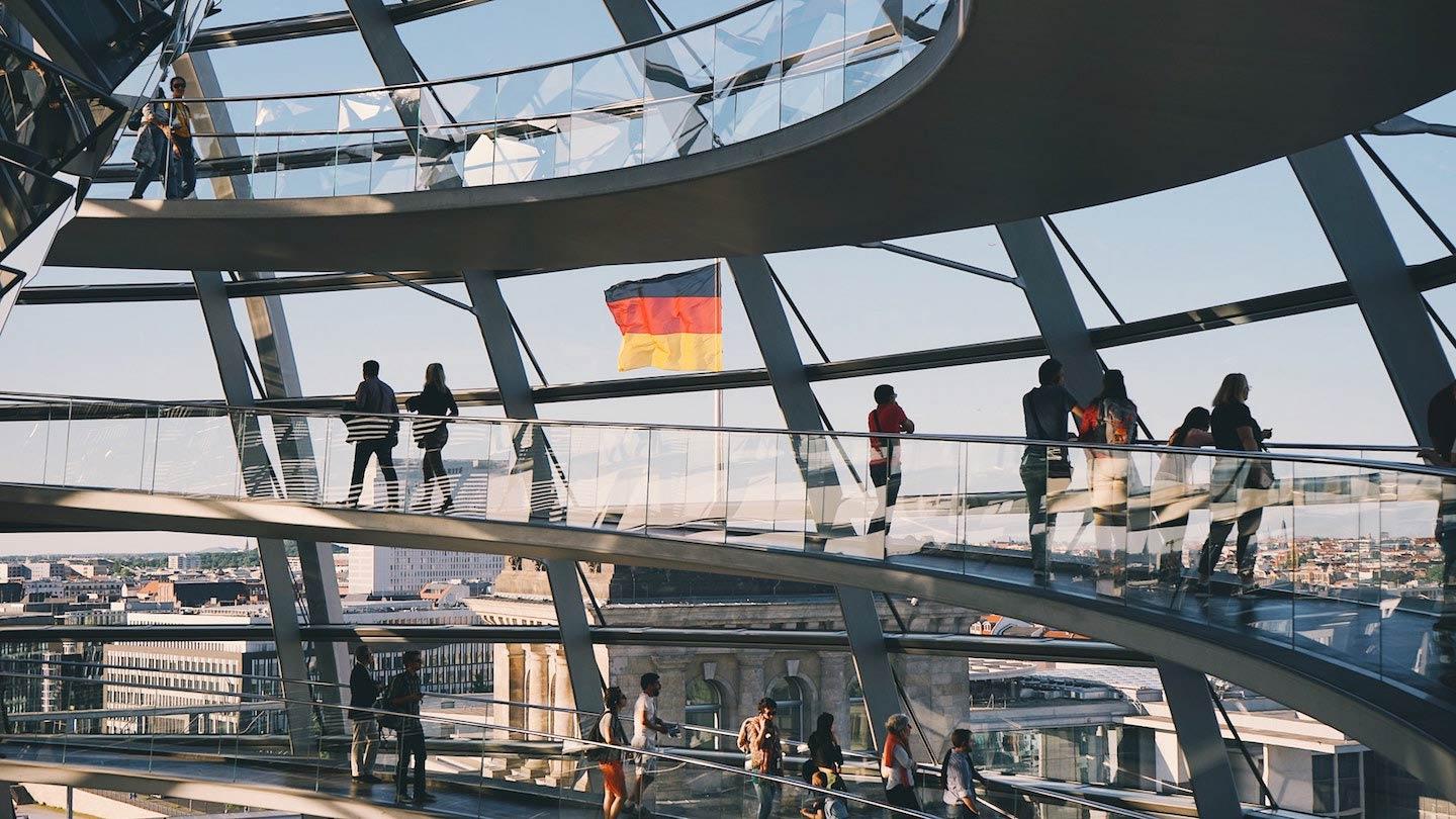 Menschen gehen in einer modernen Glaskuppel mit deutscher Flagge