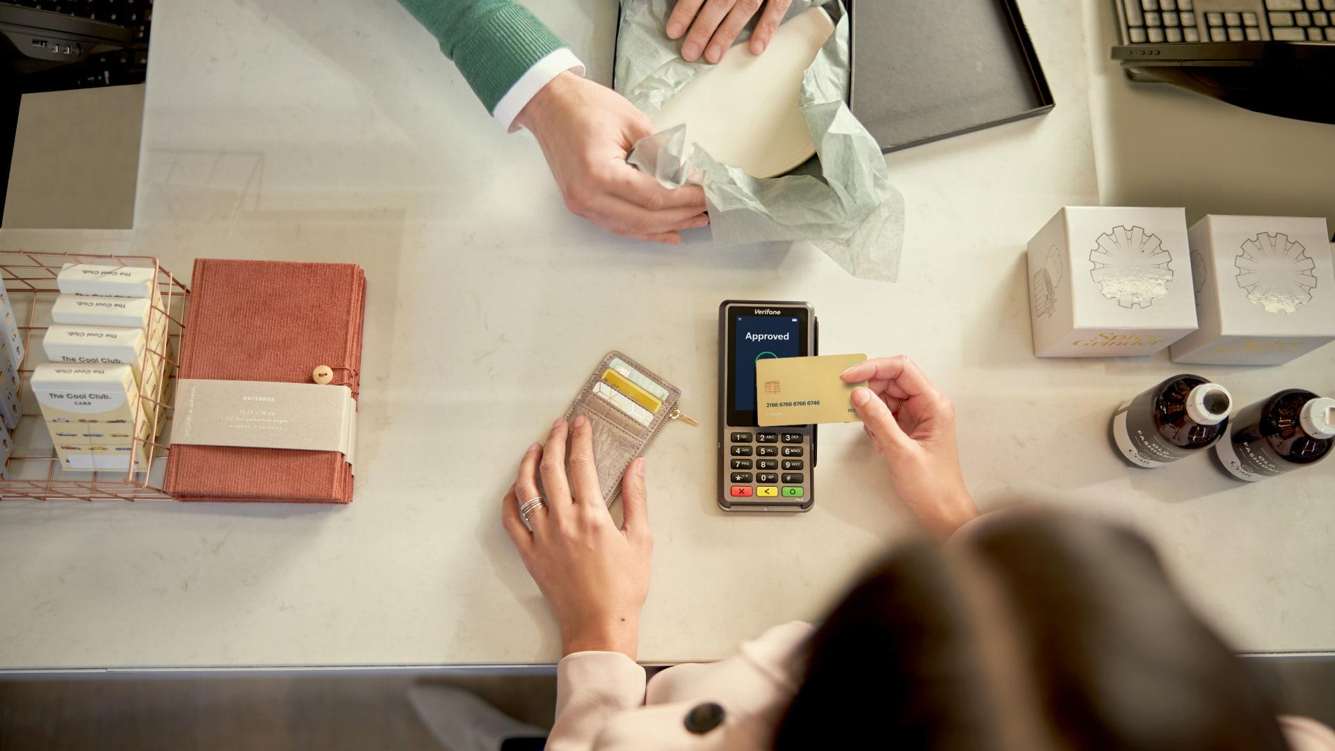 Person packaging a product and another confirming payment on an Adyen terminal displaying 'Approved'.