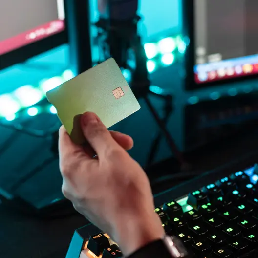 Person holding a credit card near a computer keyboard with glowing keys.