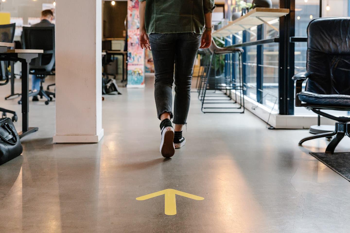 Person walking in office space following a direction arrow on the floor.
