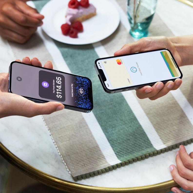 Manos sosteniendo teléfonos inteligentes cerca de un plato de postre, un teléfono muestra una aprobación de pago por Adyen.