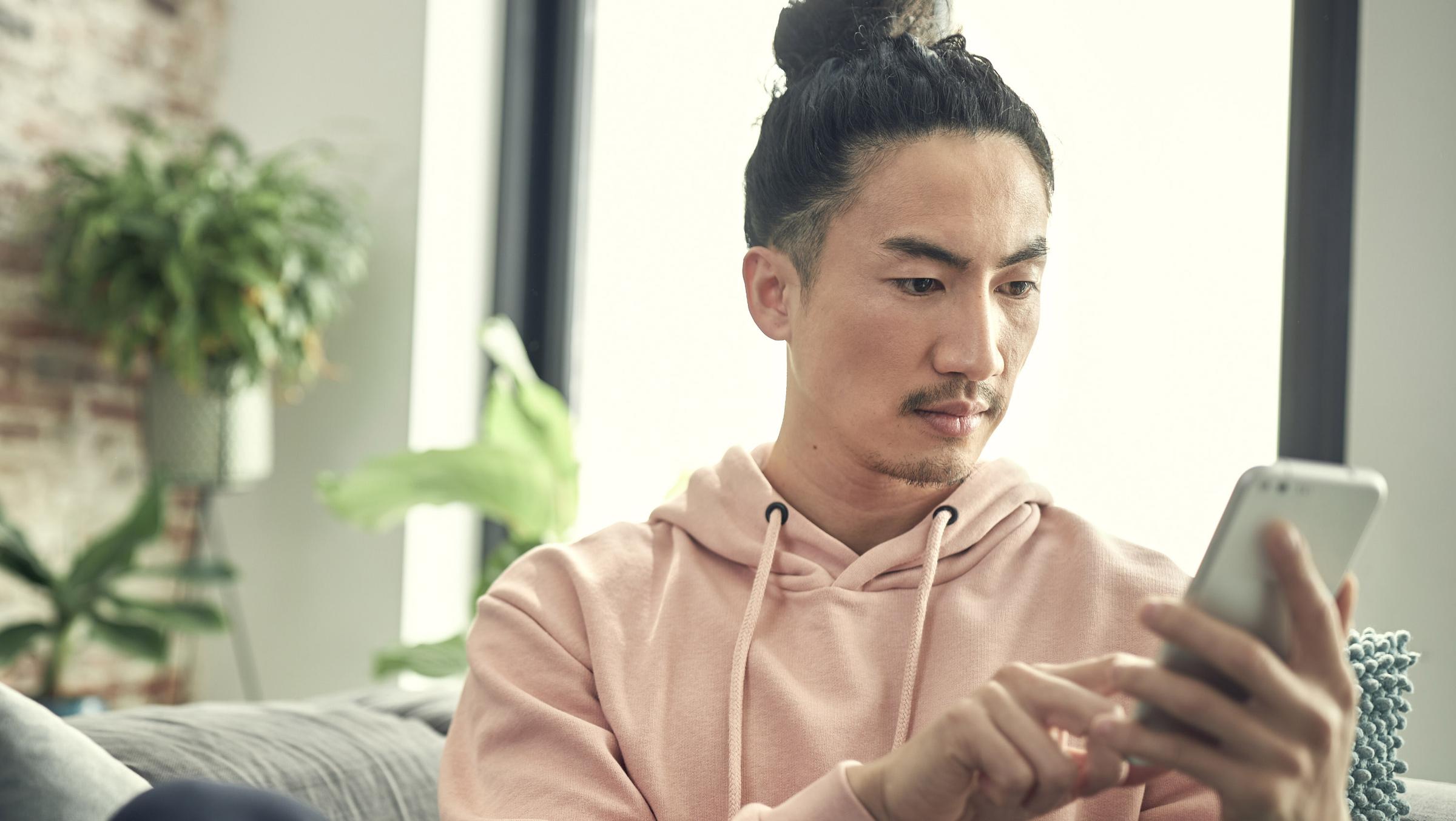 Man med manbun som bär en rosa hoodie och använder en smartphone