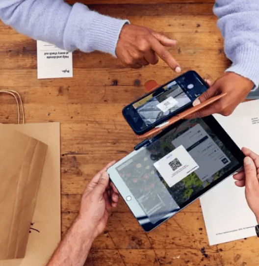 Two hands pointing at a smartphone and a tablet displaying QR code payment options.