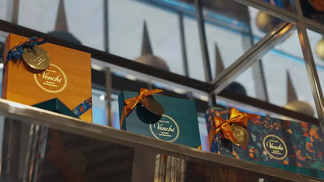 Boîtes de chocolat Venchi sur un étagère en verre avec des rubans décoratifs.