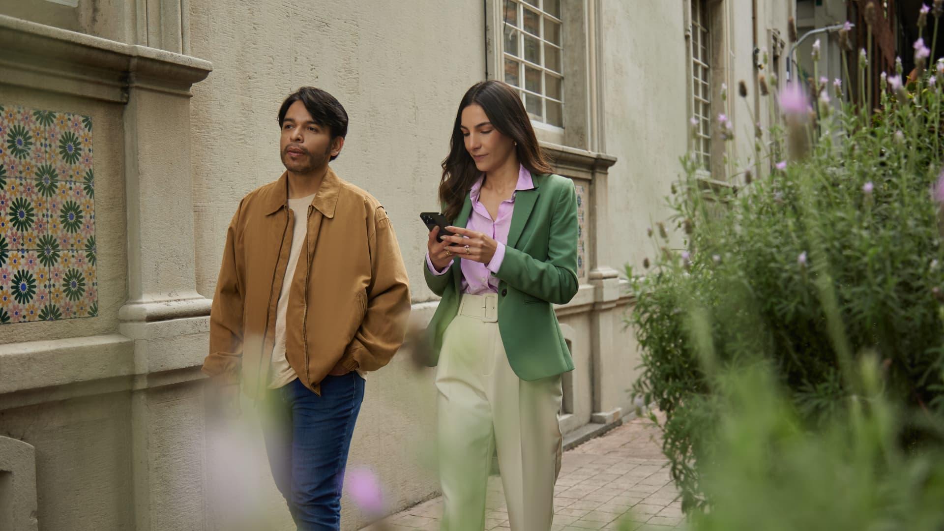 Man and woman walking down the street, woman looking at her phone.