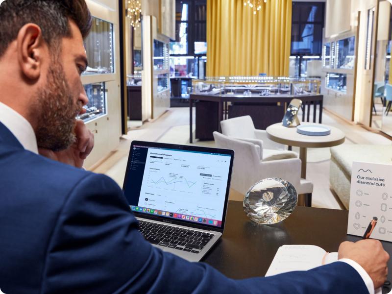 Homem analisando dados em laptop com Adyen analytics visível na tela em um ambiente de varejo de luxo