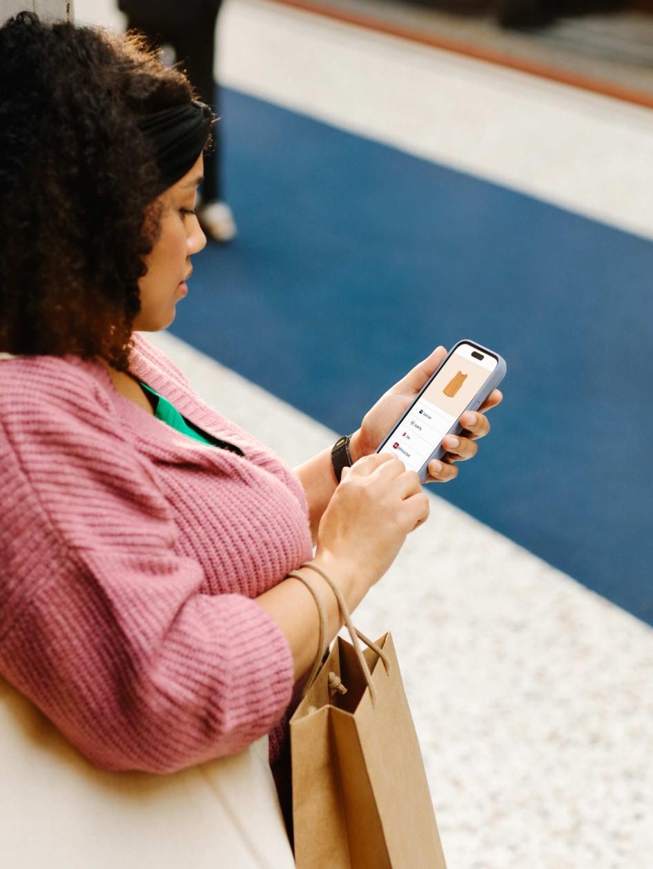 Person sitting and using a smartphone with a shopping bag beside them.