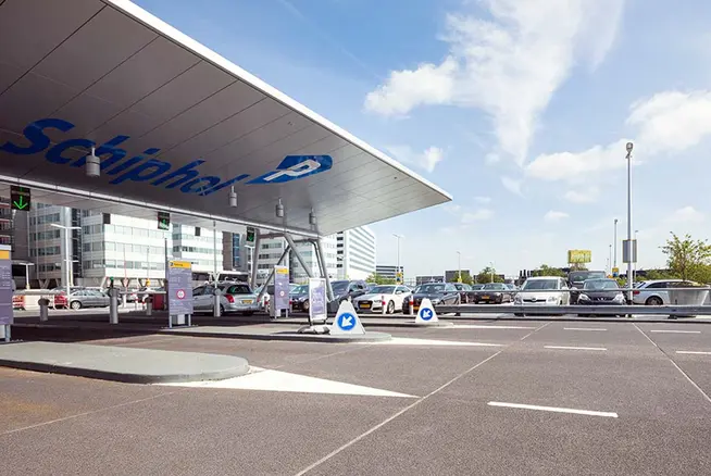 Schiphol Lufthavn parkeringsområde med biler og vejvisningsskilter under en klar himmel