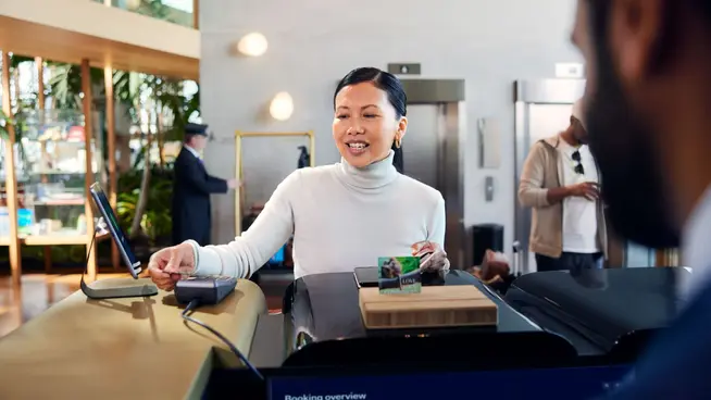 Mujer sonriendo realizando un pago sin contacto en la recepción de un hotel.