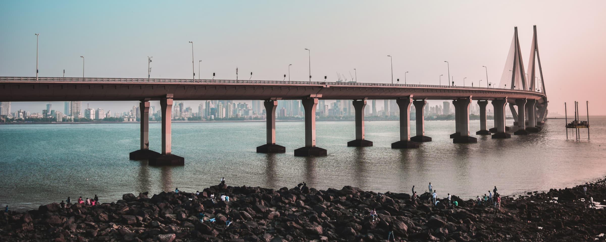 Lang hengebruksbro over et vann med byens skyline i bakgrunnen ved skumring