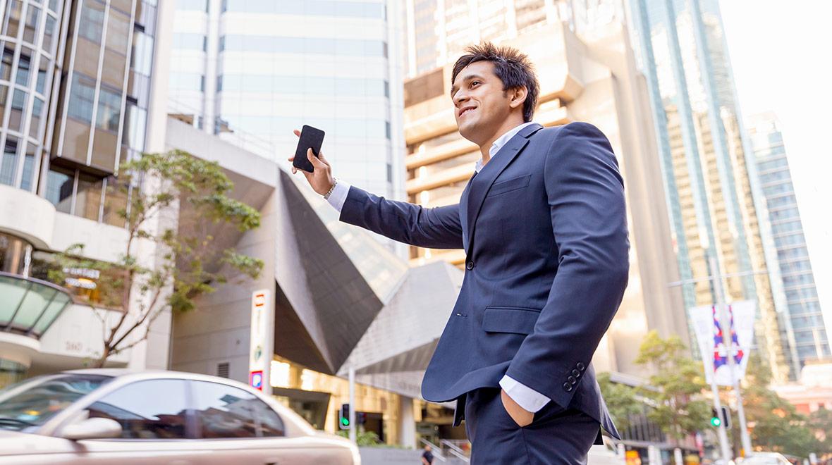 Homem de negócios sorridente de terno usando um smartphone em uma rua da cidade