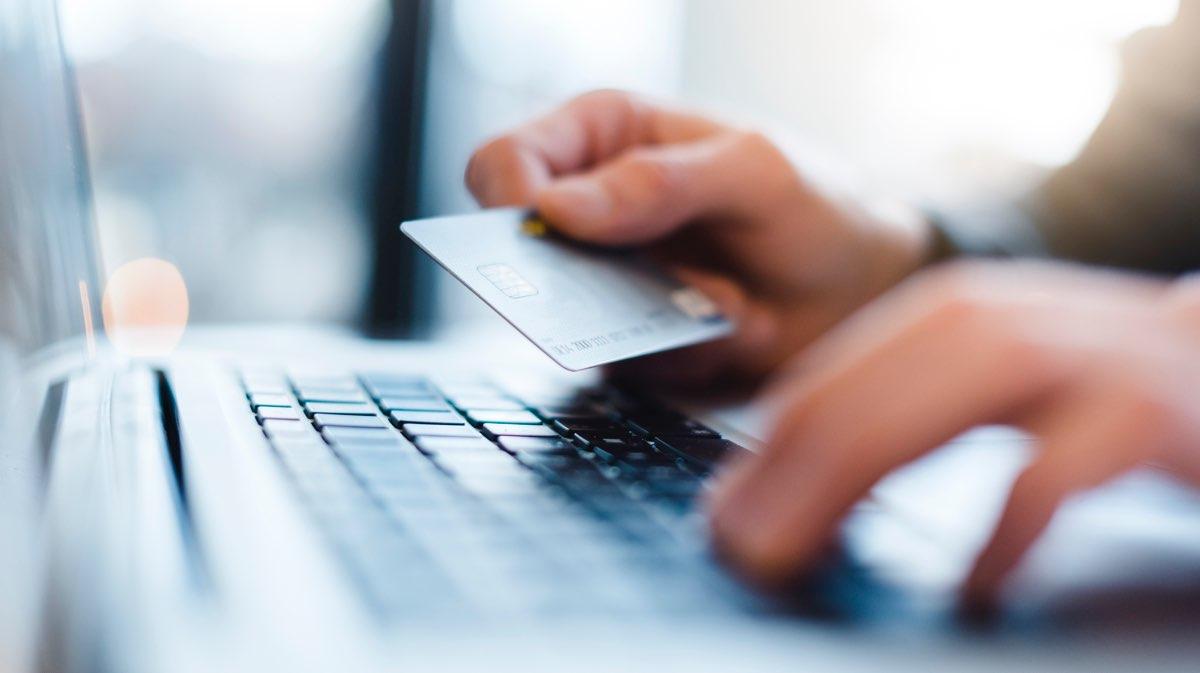 Primeiro plano de uma mão segurando um cartão de crédito sobre o teclado do laptop