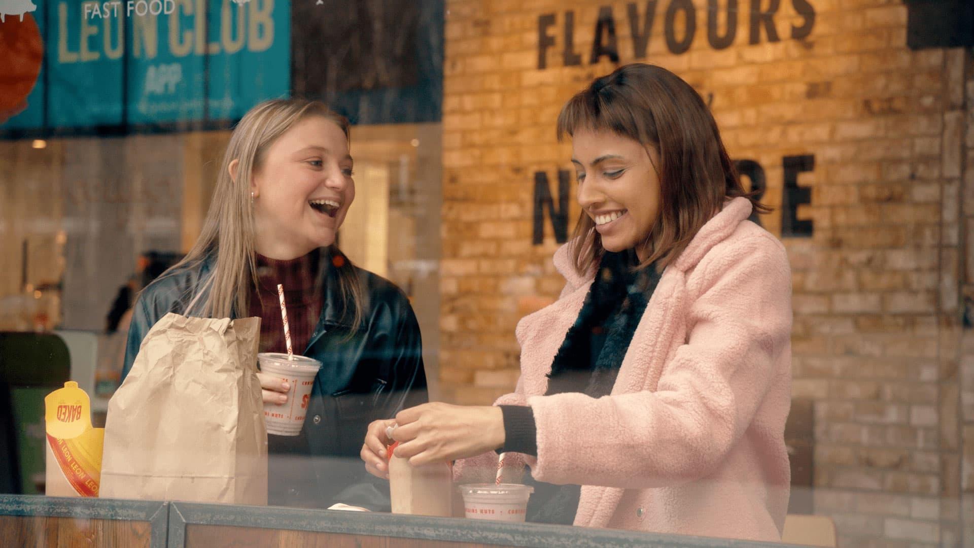 Two women smiling and enjoying beverages at a cafe with visible Adyen payment terminal.