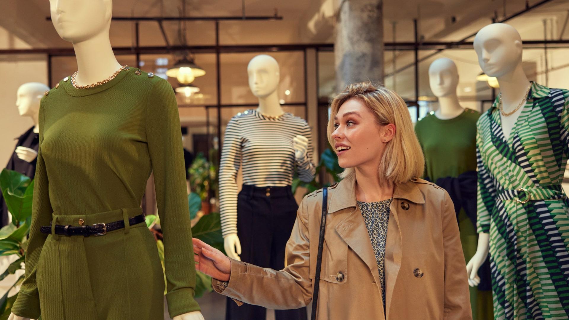 Frau shoppt und bewundert Kleidung an Mannequins in einem Geschäft