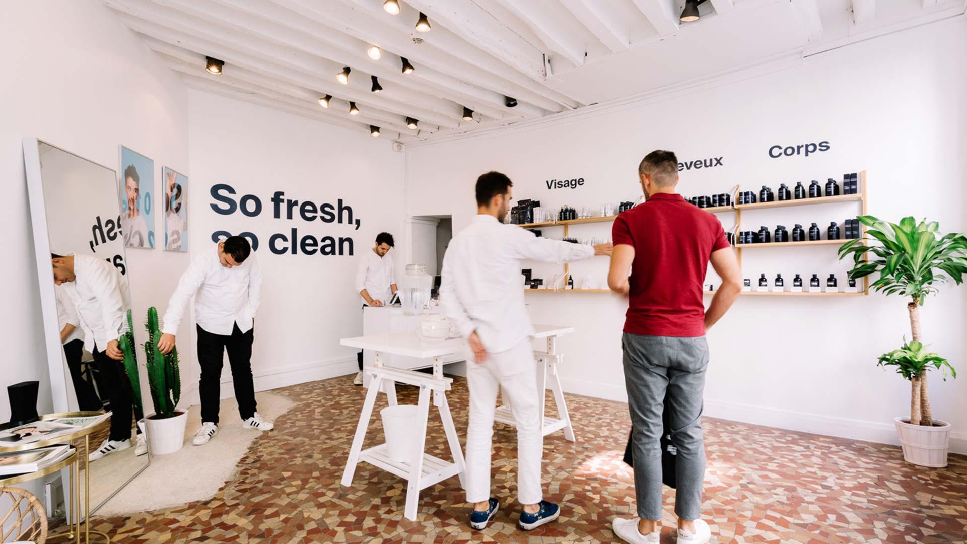 Hommes dans un magasin de produits de soins modernes avec des étagères de produits et un client en train d'être servi.