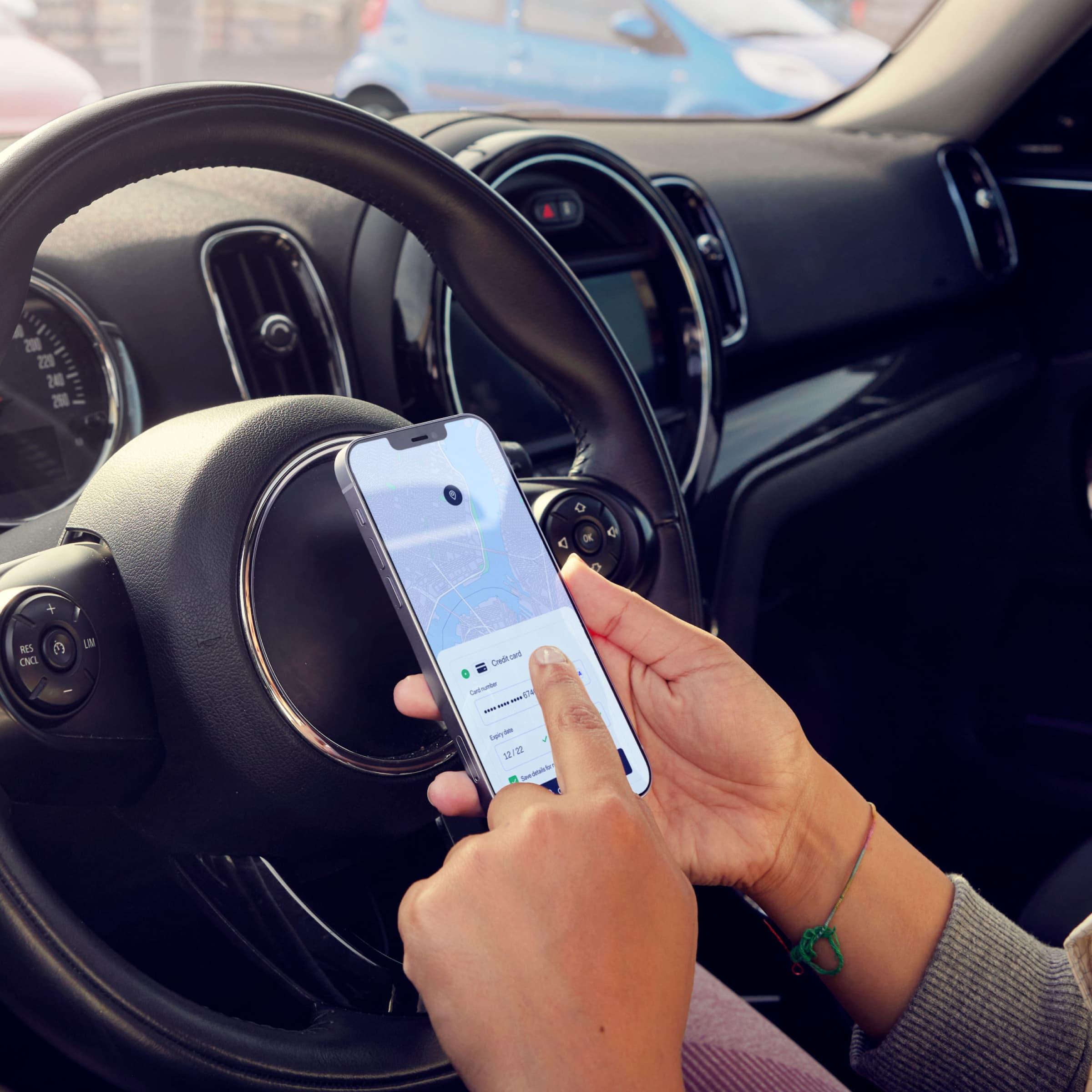 Close-up of hands holding a smartphone with a map application on the screen inside a car.