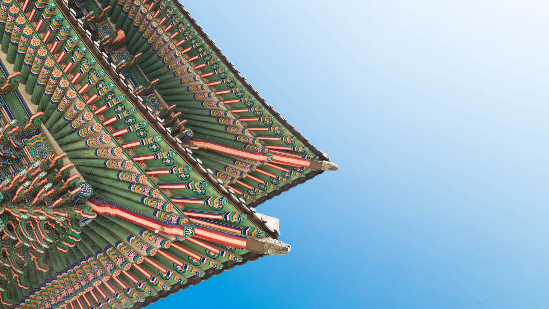 Traditional Korean temple roof with intricate multicolored patterns against a clear blue sky.