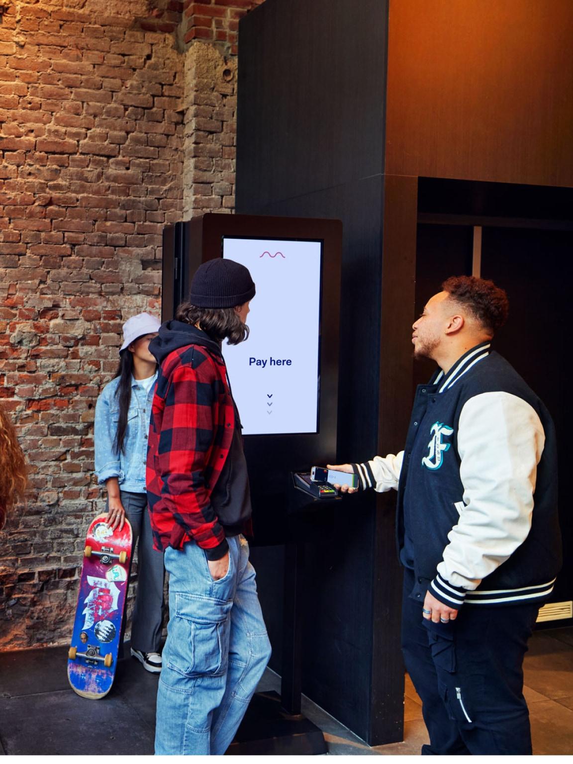 Duas pessoas em pé na frente de um terminal de pagamento Adyen com uma tela 'Pague aqui'