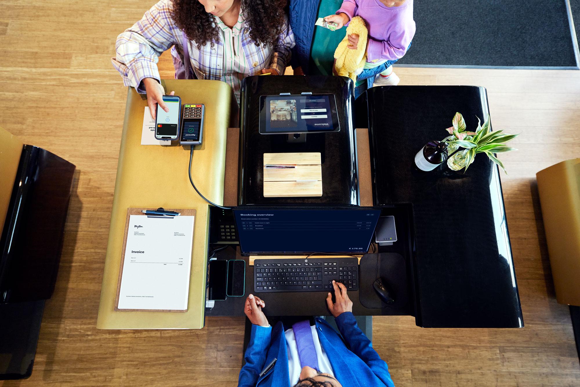A family at a hotel reception desk making a payment by tapping a smartphone at Adyen's P400 Plus terminal.