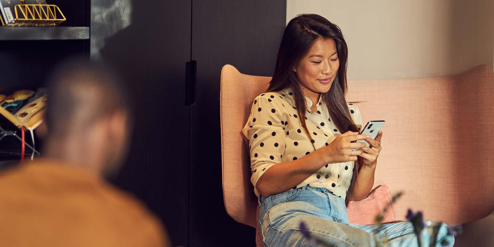 A woman sitting in an armchair browsing through her phone.