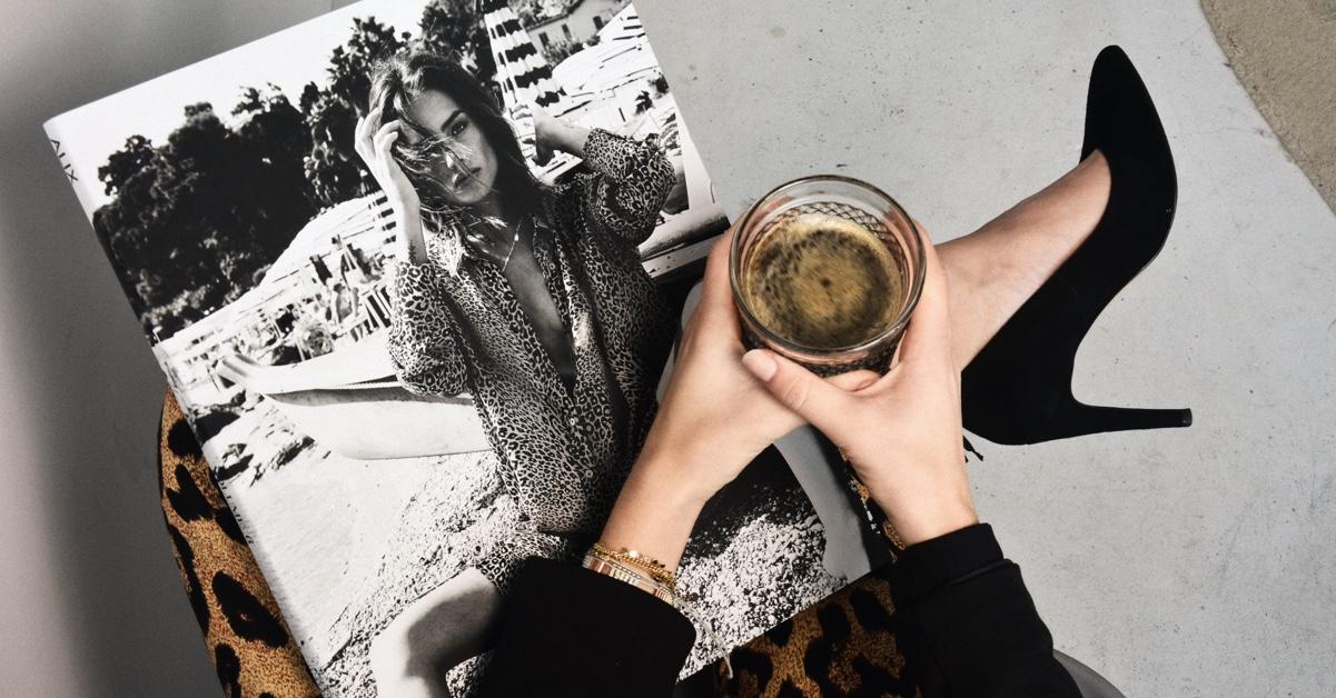 Person som holder en kopp kaffe over et magasin med et bilde av en kvinne på forsiden