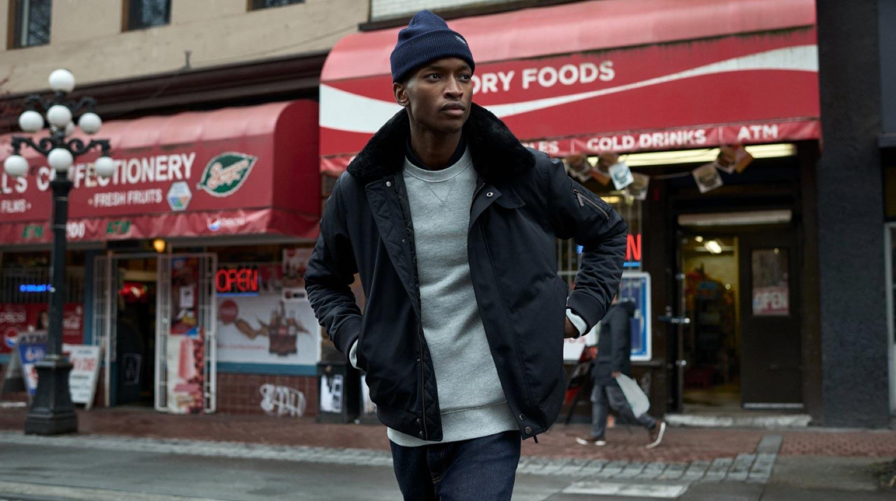 Eine Person geht vor einem Geschäft mit Geldautomat und Werbung für kalte Getränke