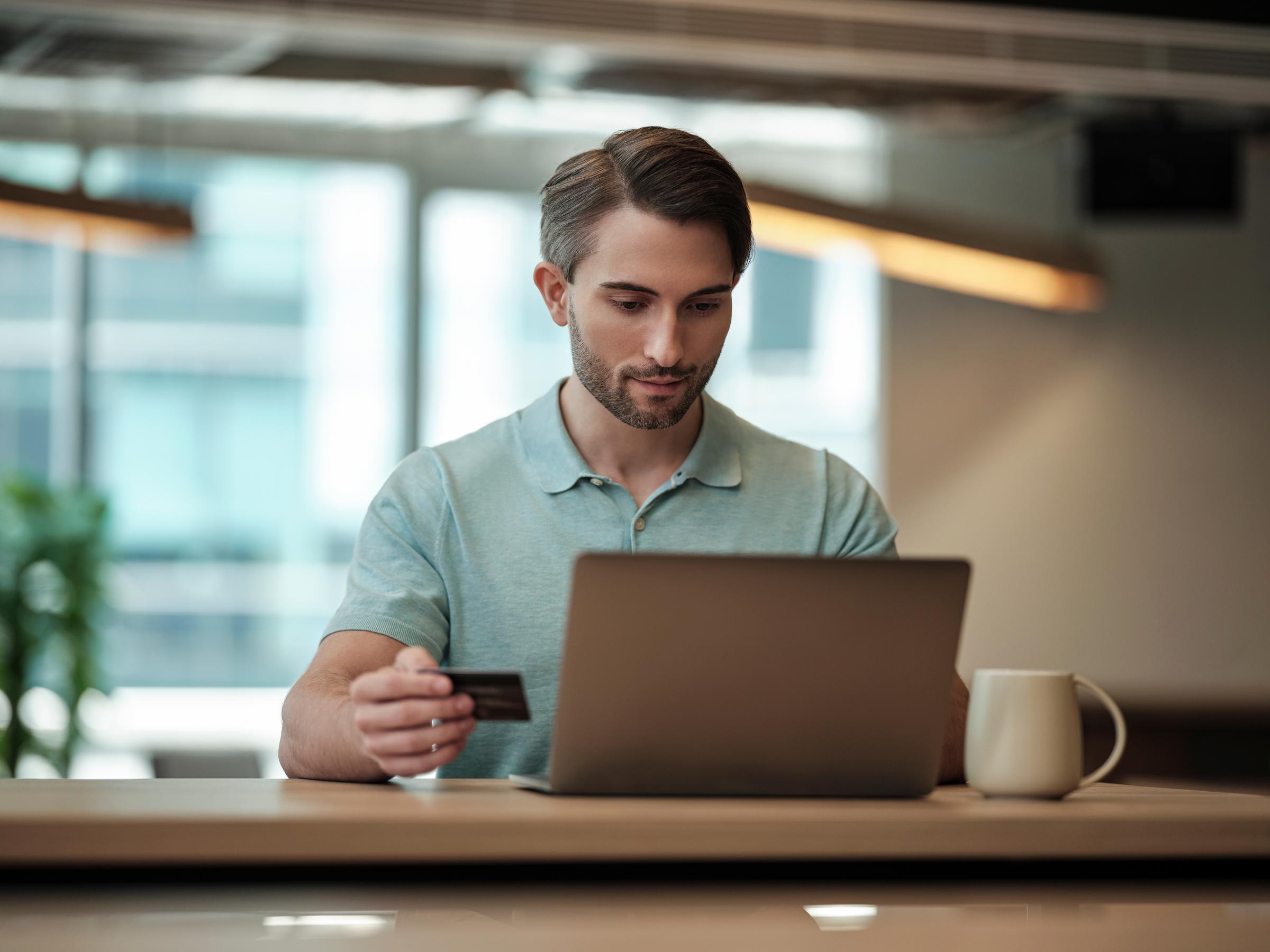 A man behind his laptop holding a payment card