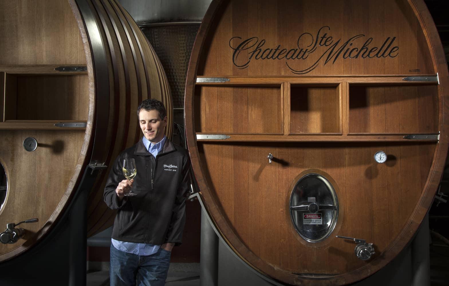 Man looking at a glass on wine in front of a wine barrel