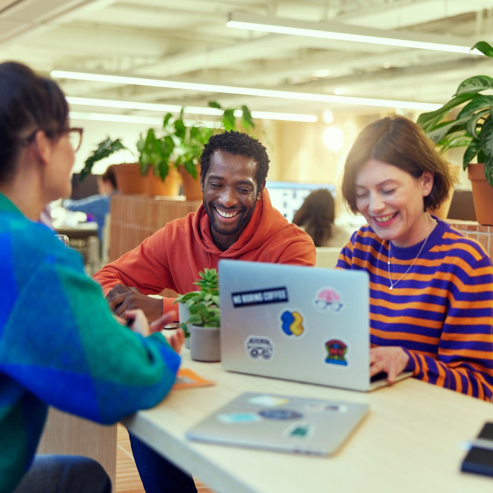 Three colleagues smiling and working together with a laptop in a modern office space.