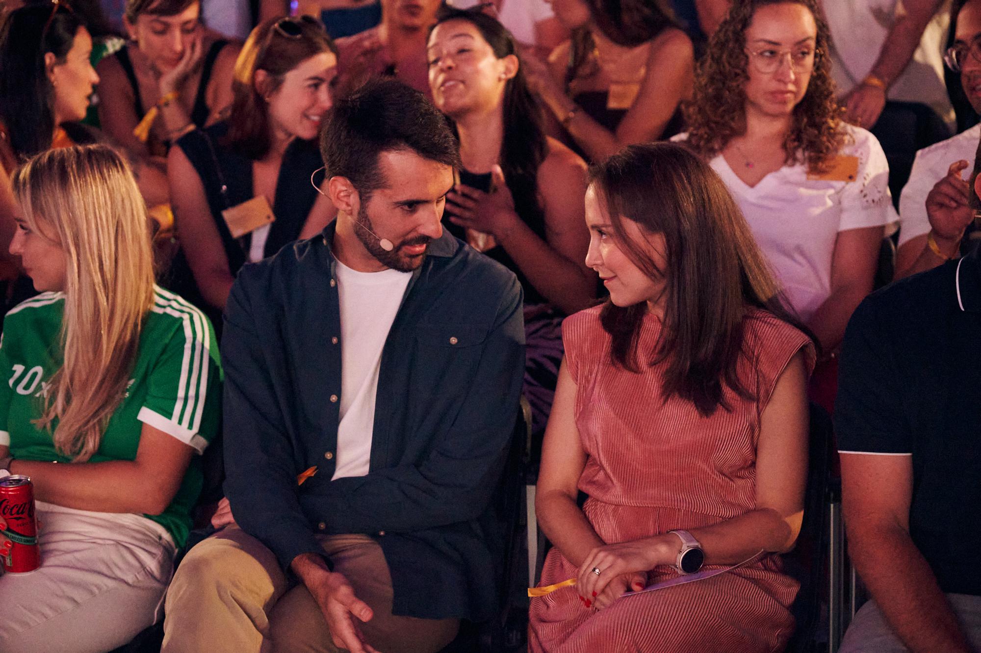 Colleagues during an event sitting in the audience talking to each other 