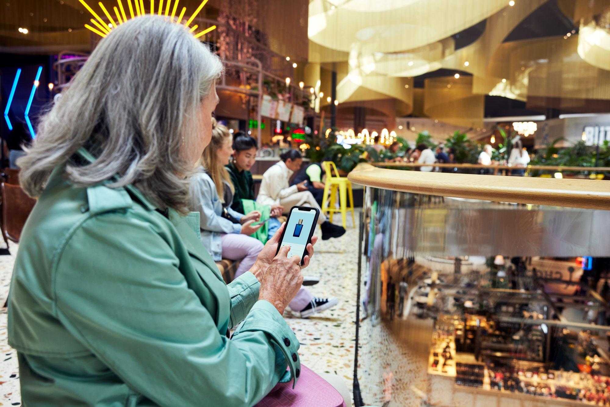 Uma mulher em um shopping comprando perfume no seu telefone.