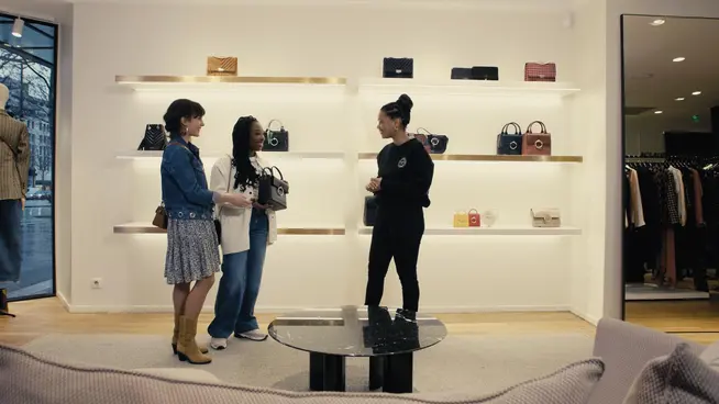 Trois personnes conversant dans une boutique moderne avec des sacs à main en vitrine.