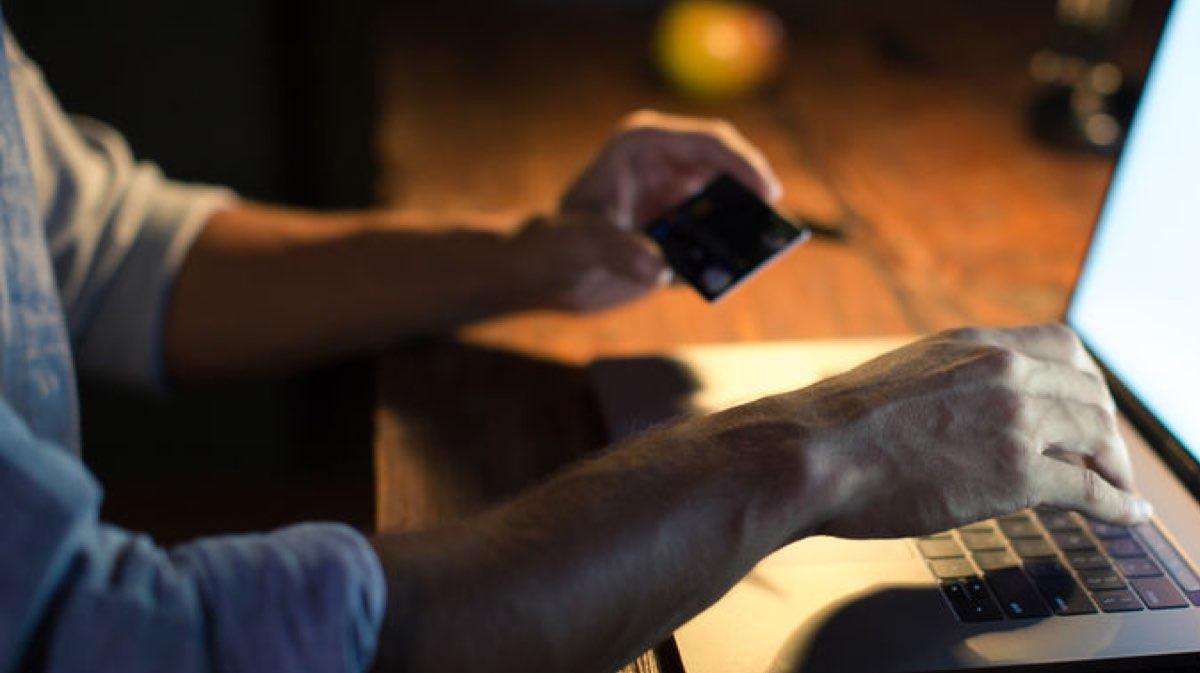 Person holding a credit card while using a laptop at night.
