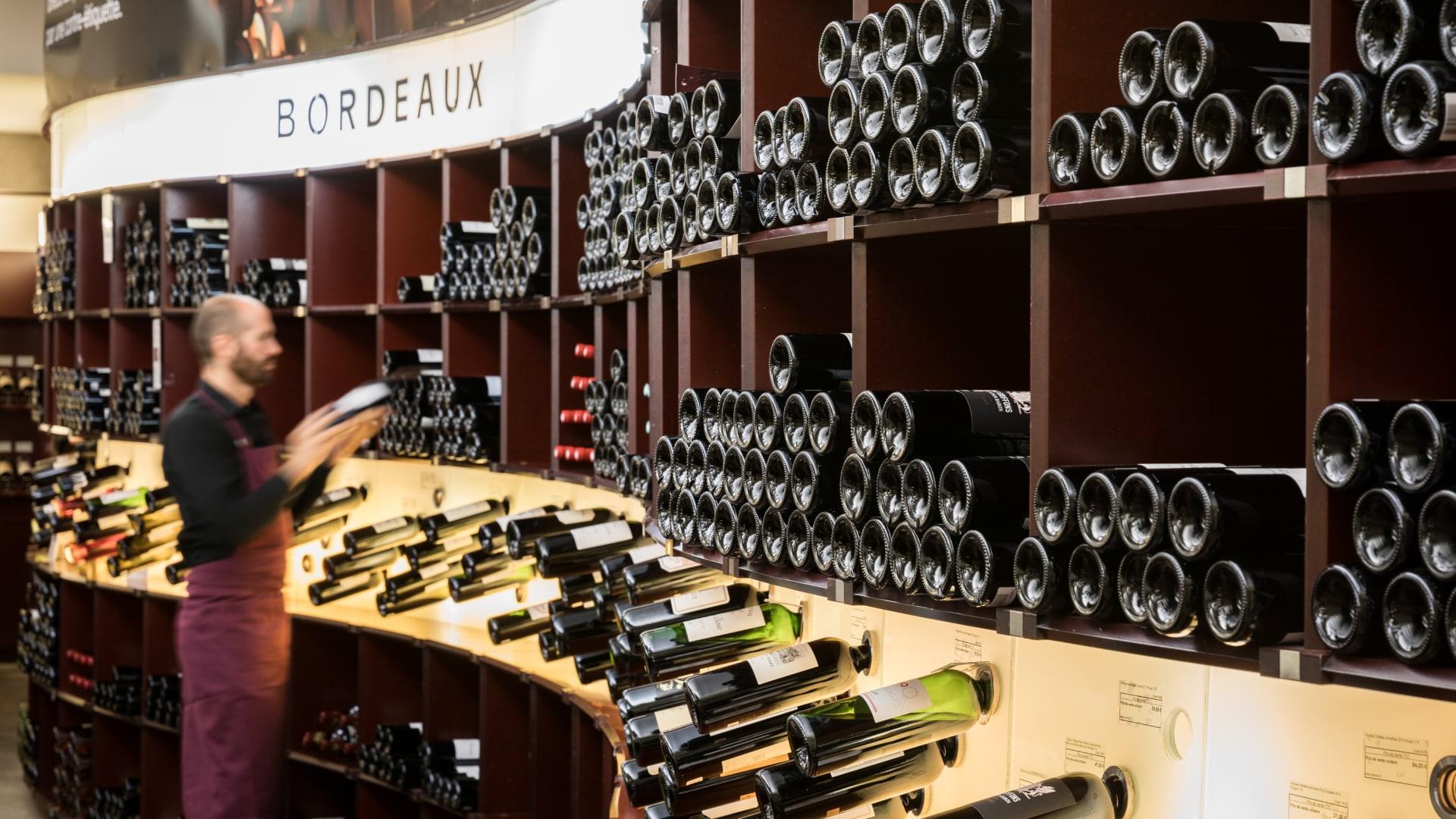 Personne rangeant des bouteilles de vin sur des étagères dans un magasin de vins étiqueté Bordeaux.