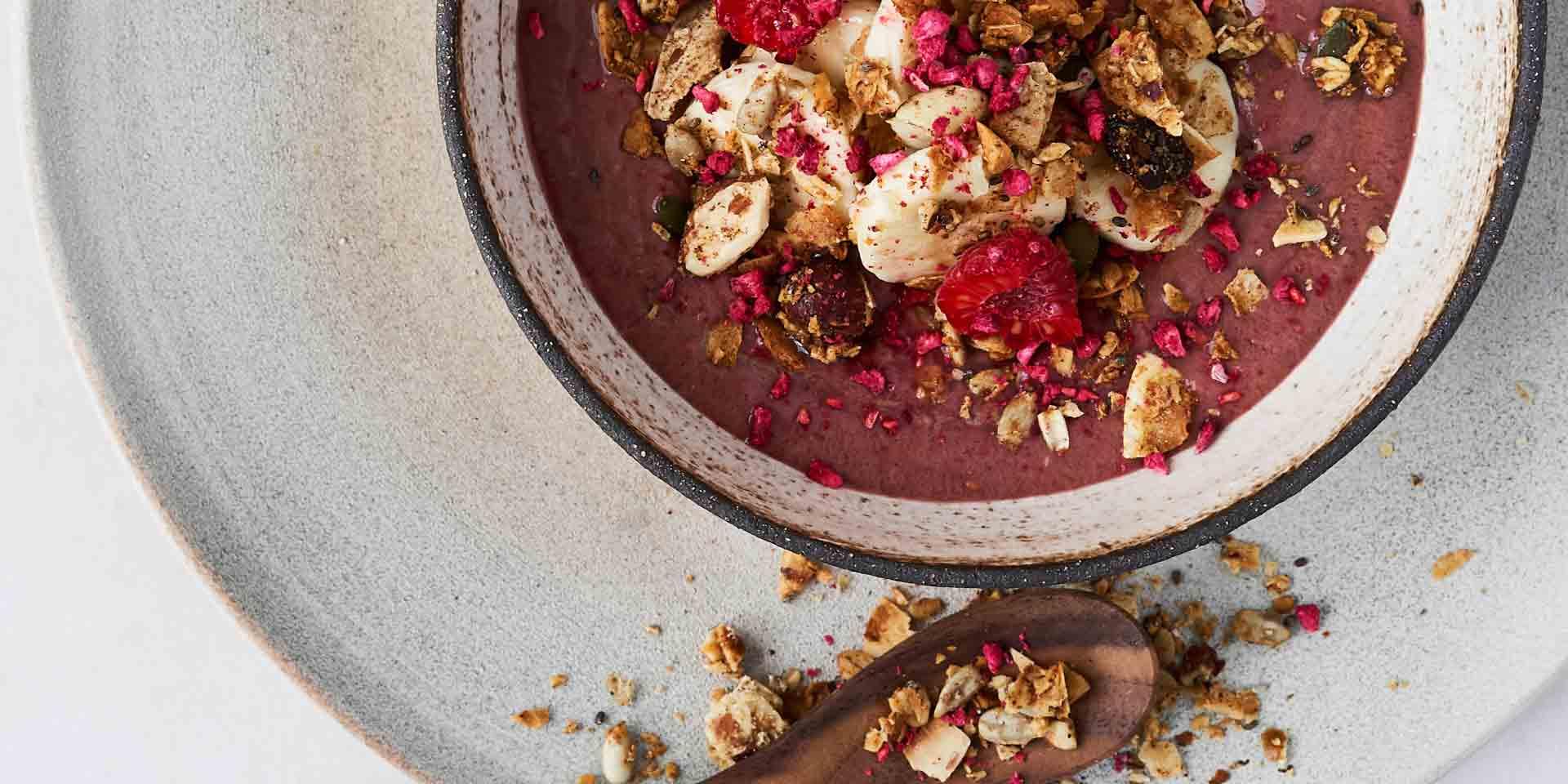 En färgglad acaibowl toppad med skivad banan, granola och frystorkade hallon.