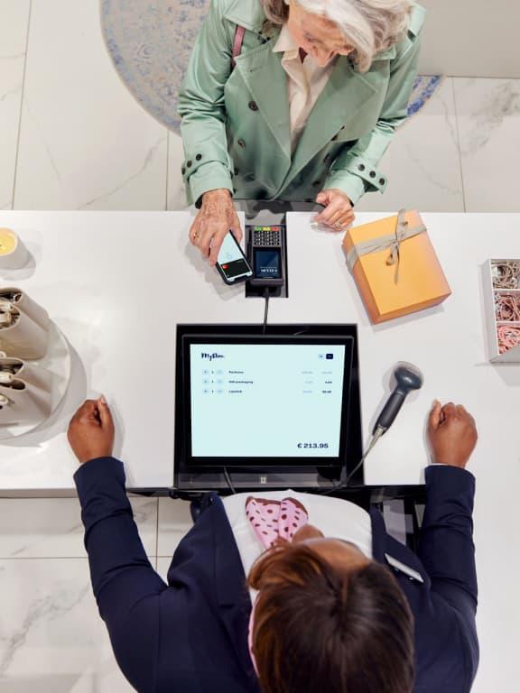 Elderly woman making a contactless payment at a store checkout with Adyen payment terminal.