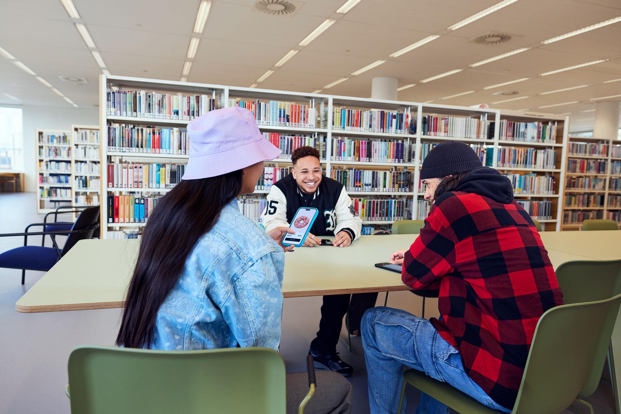 A group of young people in a library ordering donuts in a mobile application.