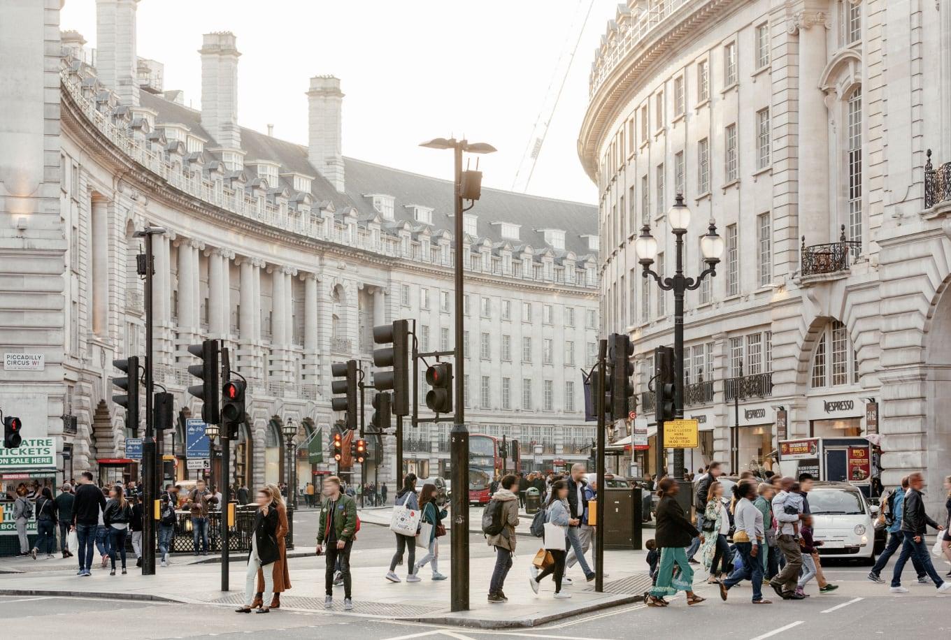 Pedestrians crossing the street in front of a curved white building in a city.