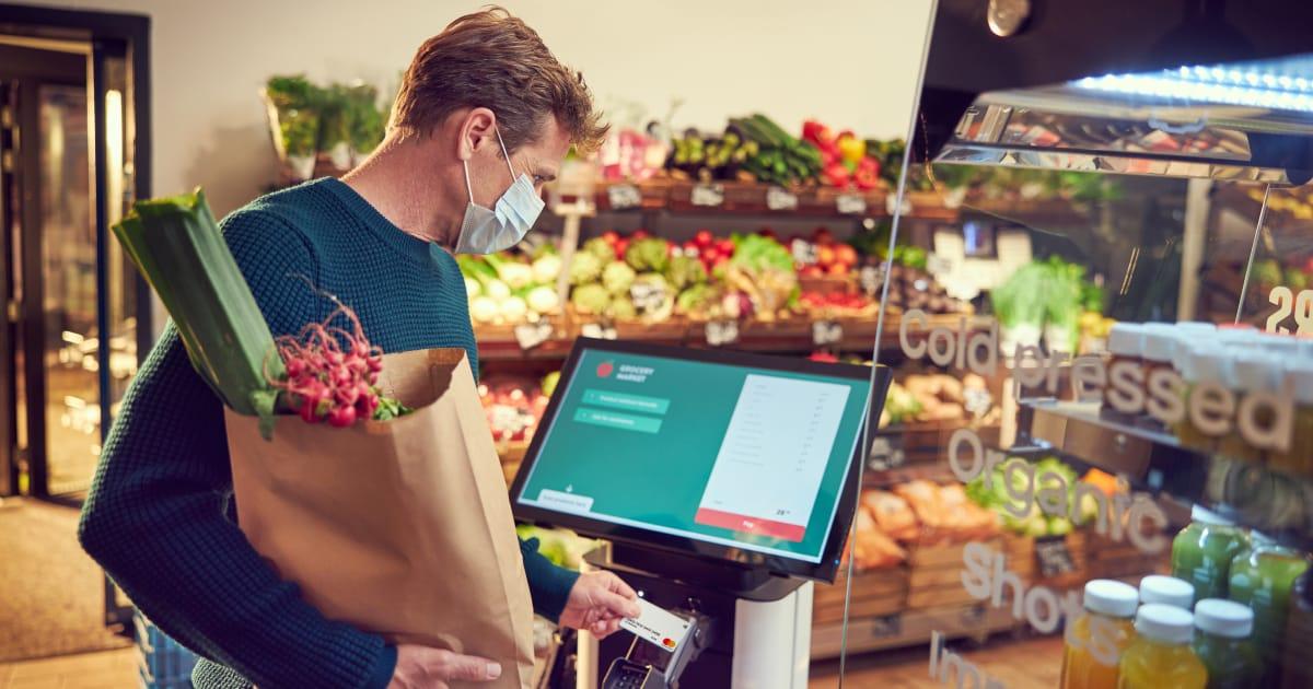 Mann mit Maske macht Zahlung an einem Selbstbedienungskiosk in einem Supermarkt