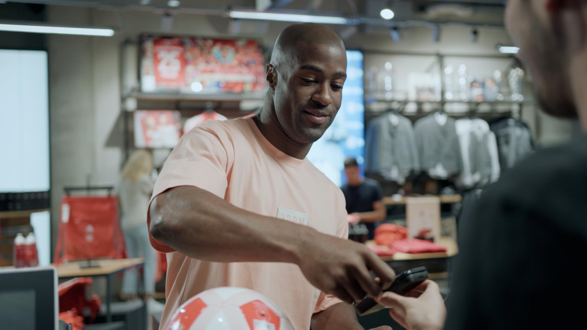 Man in peach t-shirt using mobile payment on a device in a retail store setting.