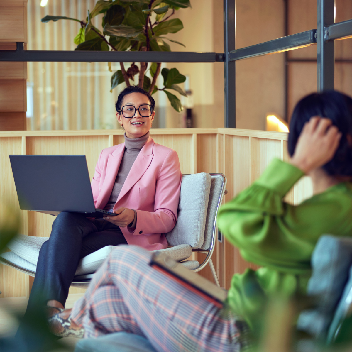 Two professionals in a modern office space, one with a laptop, engaged in conversation.