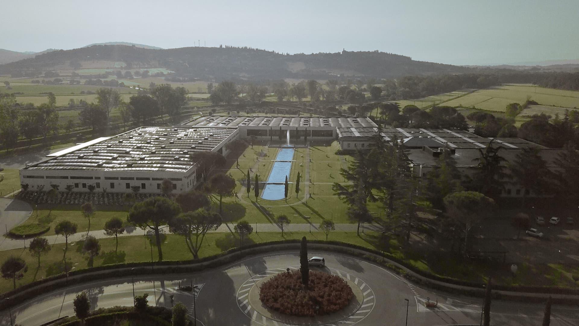 Vista aerea di un'ampia struttura con pannelli solari sui tetti circondata da alberi e campi