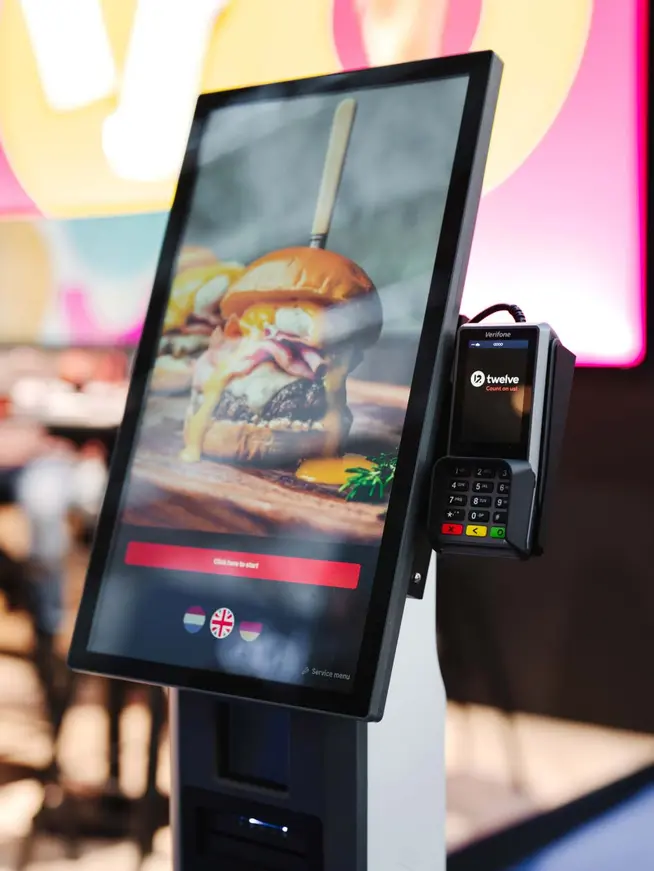 Zelfbedieningskiosk met aanraakscherm met een hamburgermenu en een gekoppelde Adyen-kaartbetalingsterminal