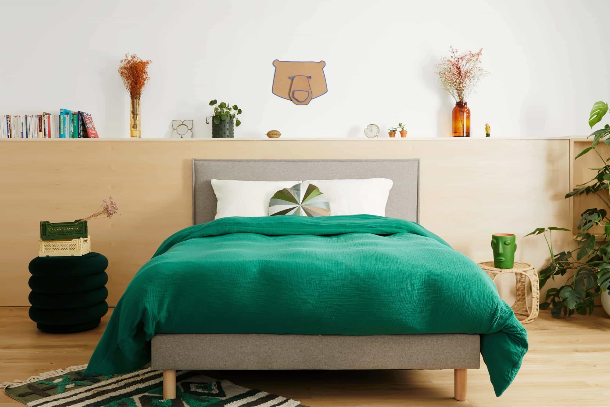 Intérieur de chambre à coucher confortable avec un lit fait avec soin, des draps verts et des plantes décoratives.