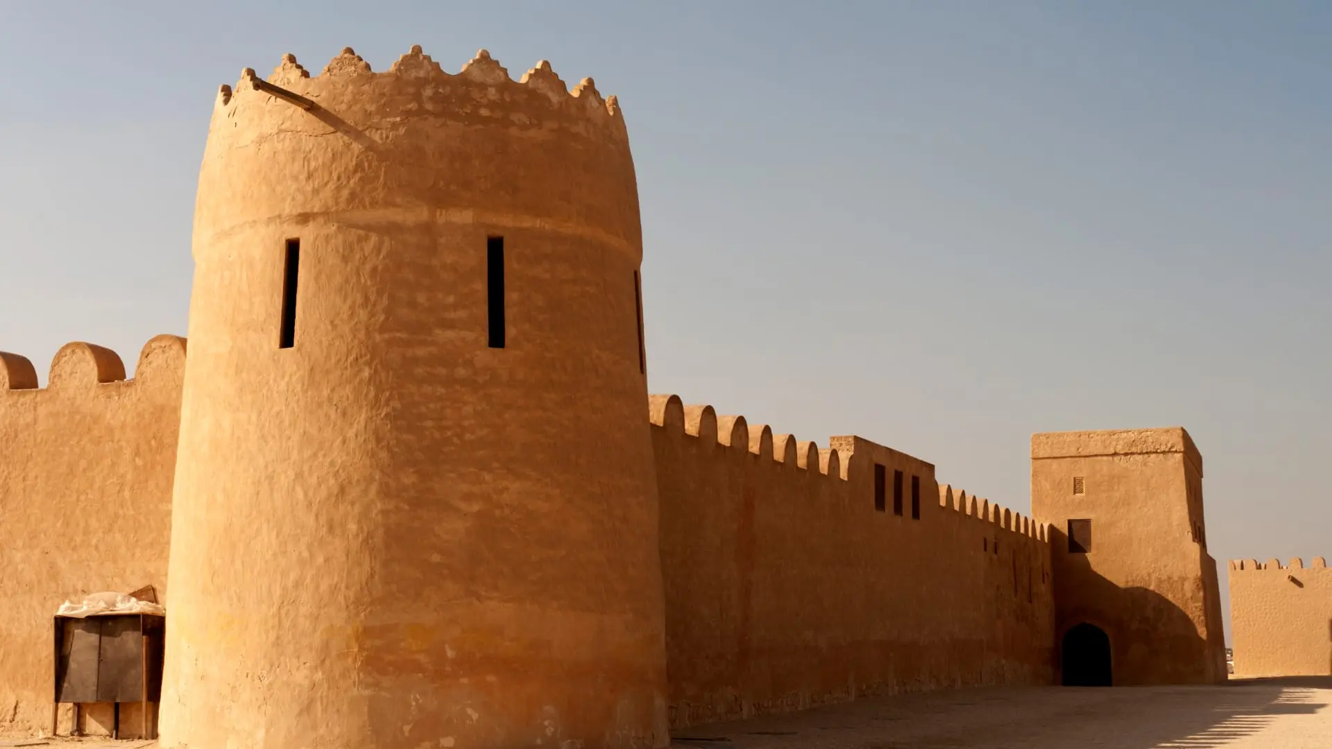 Sunlit view of a traditional earthen fortress with crenelated towers and walls in Bahrain.