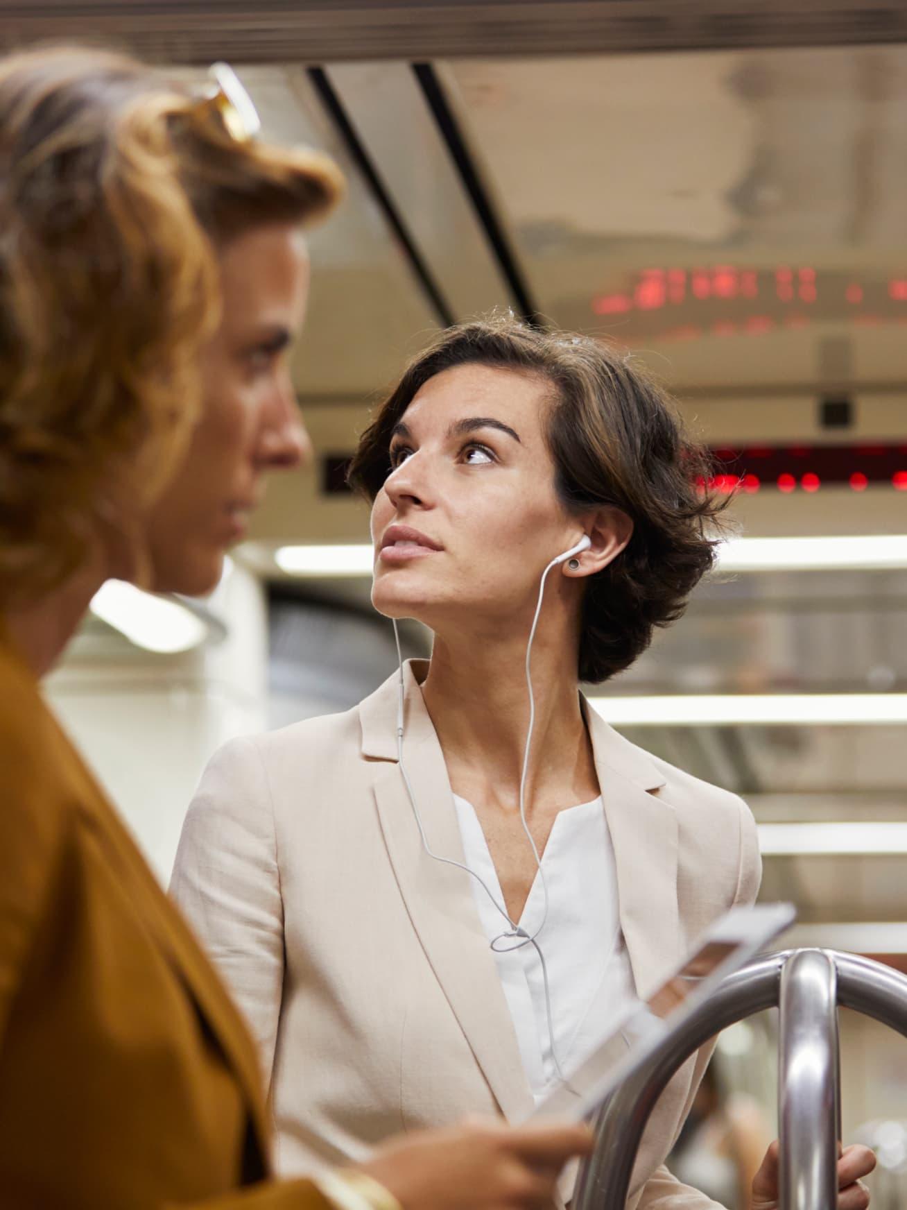 A young woman listening to music on her headphones while commuting in a subway.