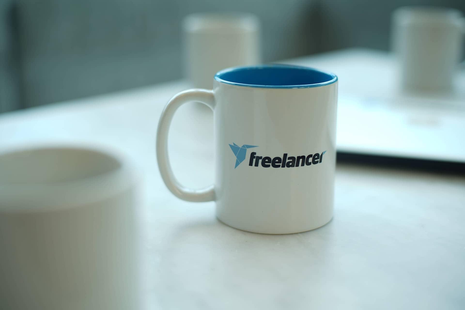 White mug with Freelancer logo on a desk.