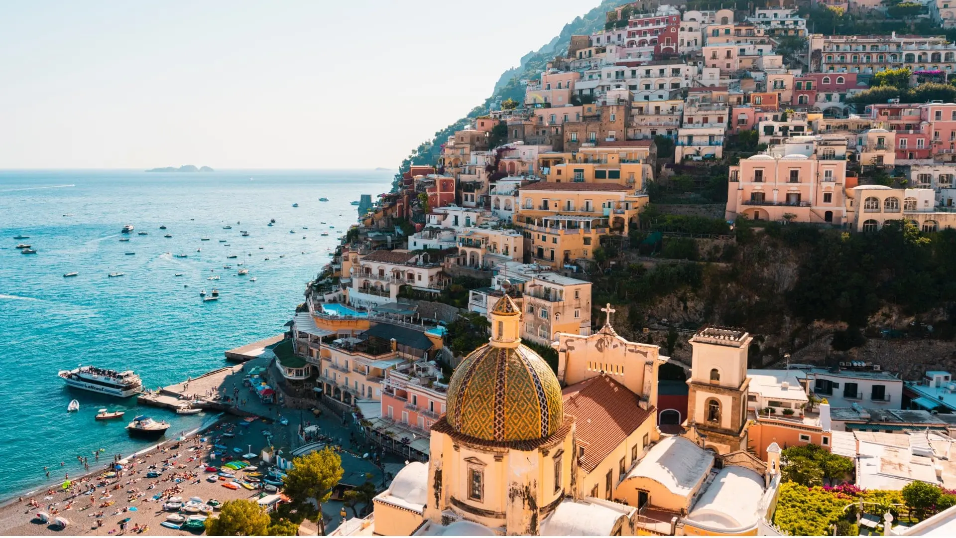 A coastal town in Italy with colorful buildings by the sea with boats and a beach.