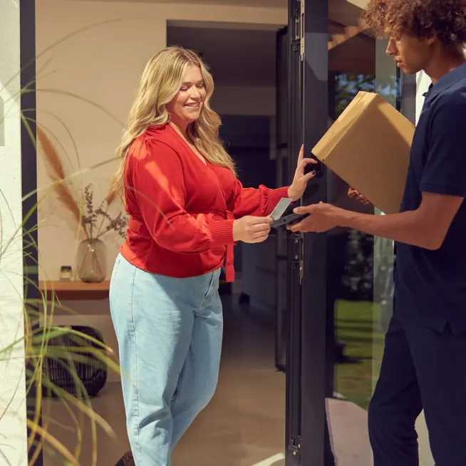 Delivery person hands over a package to a smiling woman at her doorstep.